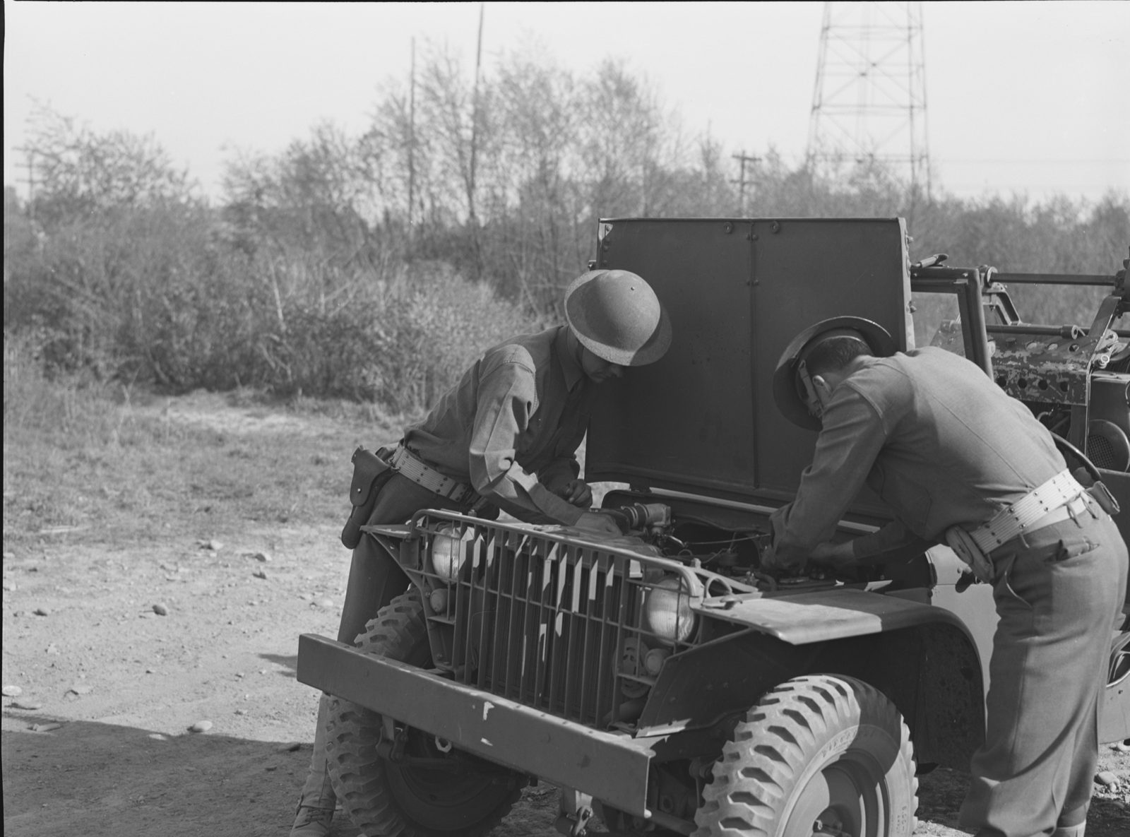 Two soldiers lean into the engine compartment of a Bantam with its hood raised against the windshield.