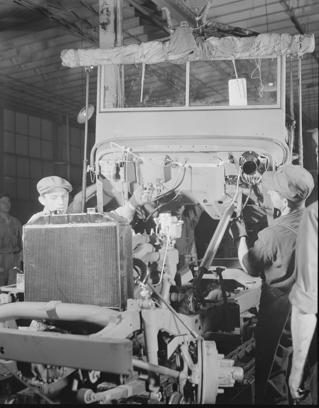 Workers on a factory line lower a jeep body onto a chassis with its radiator and engine already fitted.